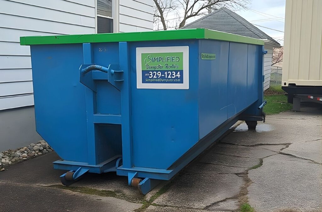 A blue Simplified Dumpster container placed beside a Lansing, MI house, offering convenient access for home renovation debris and clutter removal.